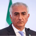 அறிக்கை வெளியிடும் ஈரானிய பட்டத்து இளவரசர் ரெசா பஹ்லவி மற்றும் பின்னணியில் ஈரான் தேசியக் கொடி.